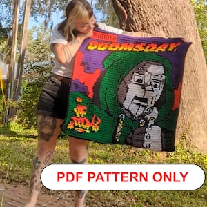 Puede incluir: Una manta cuadrada de ganchillo que presenta un retrato gráfico de una figura enmascarada con capucha verde, con el texto "DOOMSDAY" en letras amarillas en la parte superior y "RATIONS" encima. El diseño incluye acentos morados, naranjas y negros. PDF PATTERN ONLY.
