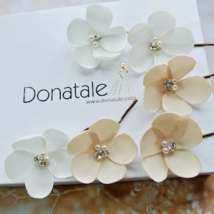 May include: Six flower hair clips with pearl and rhinestone accents. Three clips are white and three are beige.