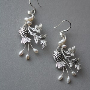 May include: Silver earrings with a thistle design and pearl accents. The thistle is a traditional Scottish symbol.