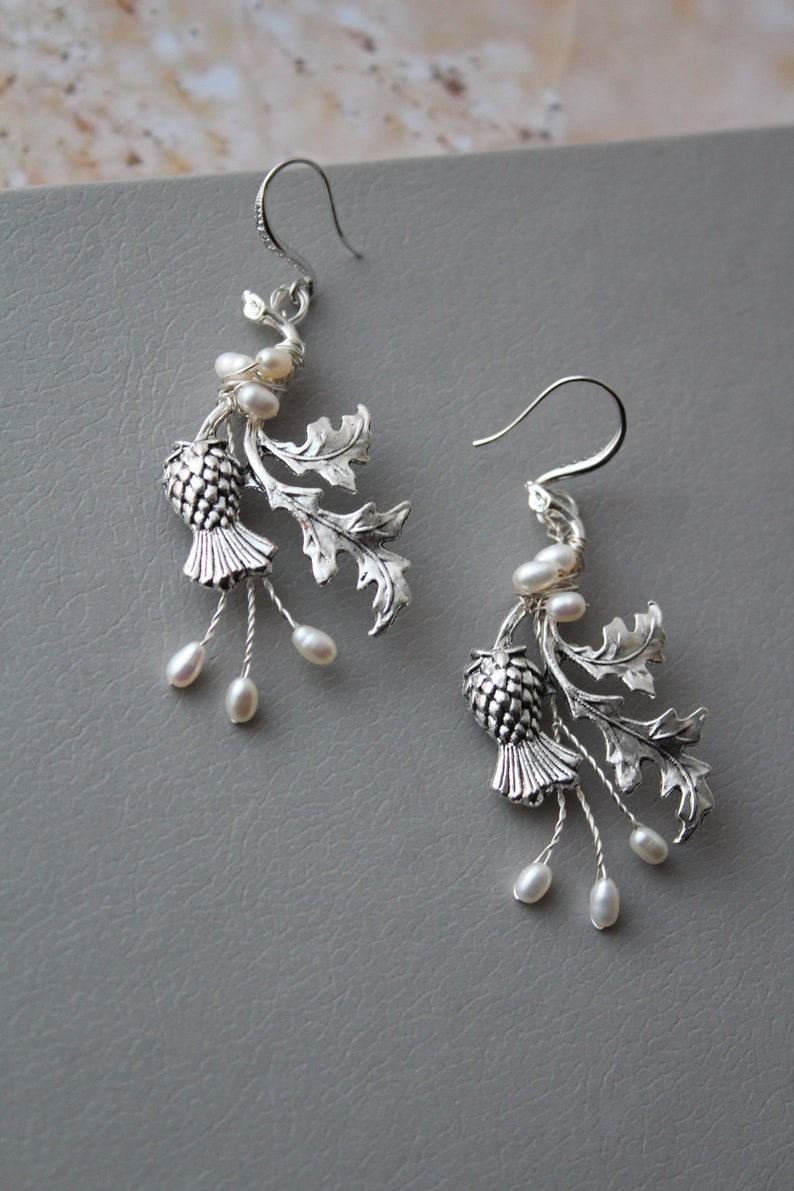 May include: Silver earrings with a thistle design and pearl accents. The thistle is a traditional Scottish symbol.