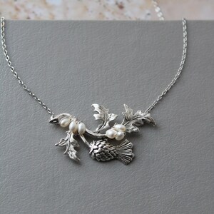 May include: A silver necklace with a thistle pendant and pearl accents. The thistle is a traditional Scottish symbol.