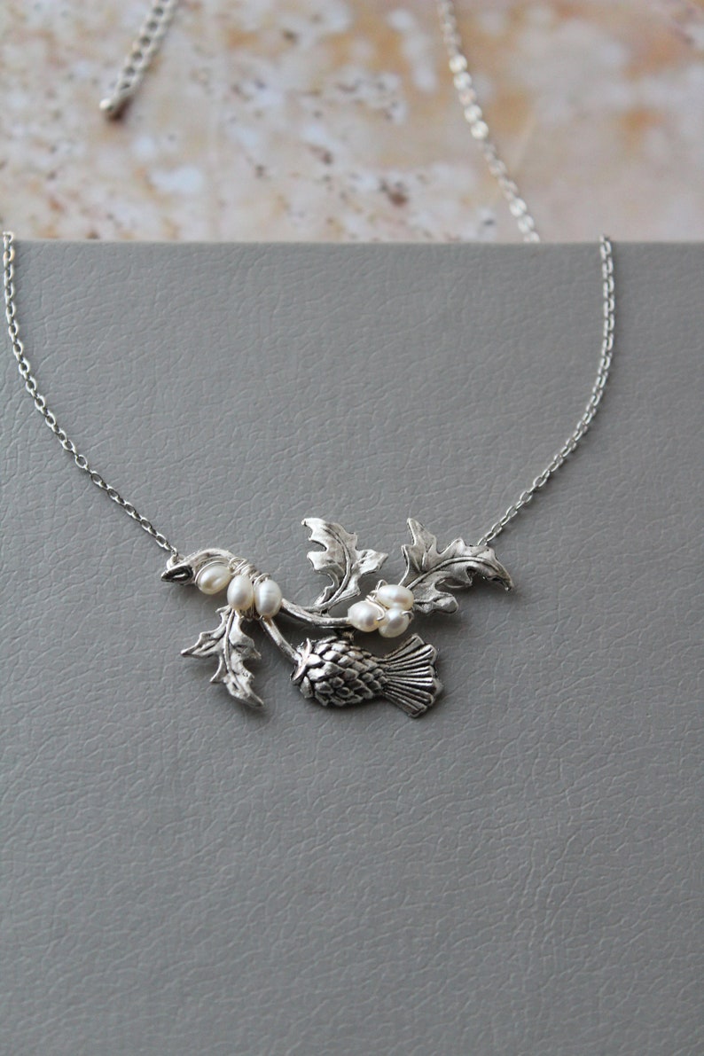 May include: A silver necklace with a thistle pendant and pearl accents. The thistle is a traditional Scottish symbol.