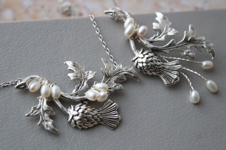 May include: Silver necklace with two thistle pendants and pearl accents. The thistle is a traditional Scottish symbol.