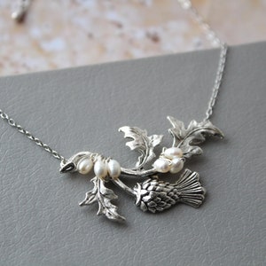 May include: A silver necklace with a thistle pendant and pearl accents. The thistle is a traditional Scottish symbol.