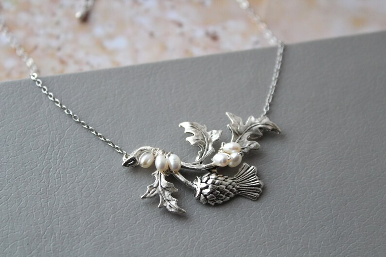May include: A silver necklace with a thistle pendant and pearl accents. The thistle is a traditional Scottish symbol.