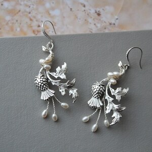 May include: Silver earrings with a thistle design and pearl accents.