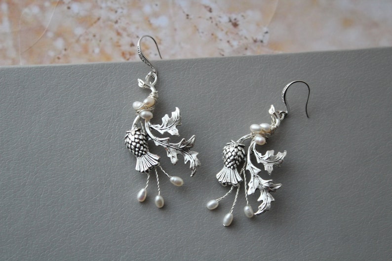 May include: Silver earrings with a thistle design and pearl accents.