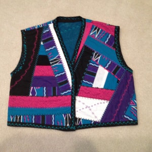 Puede incluir: Un chaleco sin mangas hecho de tela de patchwork. El chaleco est&aacute; hecho de telas de diferentes colores, incluyendo negro, rosa, azul, morado y blanco. El chaleco tiene un borde festoneado.