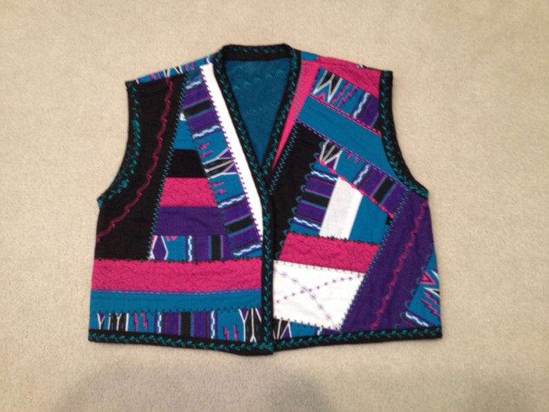 Puede incluir: Un chaleco sin mangas hecho de tela de patchwork. El chaleco est&aacute; hecho de telas de diferentes colores, incluyendo negro, rosa, azul, morado y blanco. El chaleco tiene un borde festoneado.