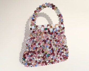 May include: A small, beaded handbag with a colorful, multi-colored design. The bag is made of small, round beads in shades of pink, purple, blue, green, and white.