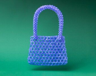 May include: A small, lavender-colored beaded handbag with a top handle.
