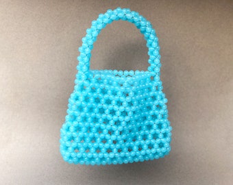 May include: A small, light blue beaded handbag with a woven design. The bag has a single handle.