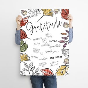Peut inclure: Une affiche imprimable blanche avec un motif dessin&eacute; &agrave; la main de feuilles d'automne dans des tons de rouge, orange, jaune et vert. L'affiche pr&eacute;sente le mot "Gratitude" en &eacute;criture cursive noire et une liste de choses pour lesquelles &ecirc;tre reconnaissant, notamment "Ma grand-m&egrave;re", "Dinde", "Mes cousins", "Famille", "Petits-enfants", "Tarte aux pommes", "Mon chiot", "Soleil", "Faire du v&eacute;lo sans roulettes", "Ma s&oelig;ur" et "Promenades dans les bois".