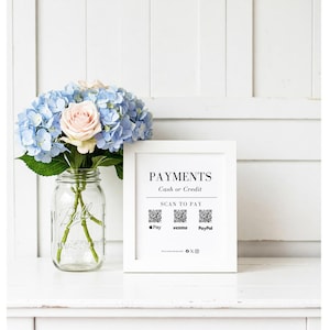 May include: A white framed sign with the word "PAYMENTS" in black text, along with "Cash or Credit" and "SCAN TO PAY". Below are QR codes for Pay, Venmo, and PayPal. A bouquet of blue hydrangeas and a pink rose are in a glass jar.