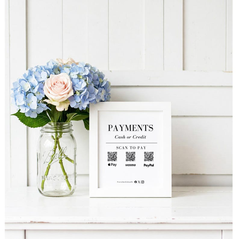 May include: A white framed sign with the word "PAYMENTS" in black text, along with "Cash or Credit" and "SCAN TO PAY". Below are QR codes for Pay, Venmo, and PayPal. A bouquet of blue hydrangeas and a pink rose are in a glass jar.