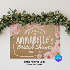 Peut inclure: Panneau rectangulaire avec le texte "Welcome to Annabelle's Bridal Shower" en blanc, entouré d'accents floraux roses. Le panneau est décoré d'une guirlande de feuilles vertes et de petites lumières. La date "April 25, 2028" est également affichée.