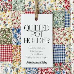 Könnte beinhalten: Ein gesteppter Topflappen mit einem Patchwork-Design aus Blumen- und Vichy-Mustern in Rot, Blau, Grün und Weiß. Das Etikett lautet "QUILTED POT HOLDER" und enthält Pflegehinweise. Handgemacht mit Liebe.