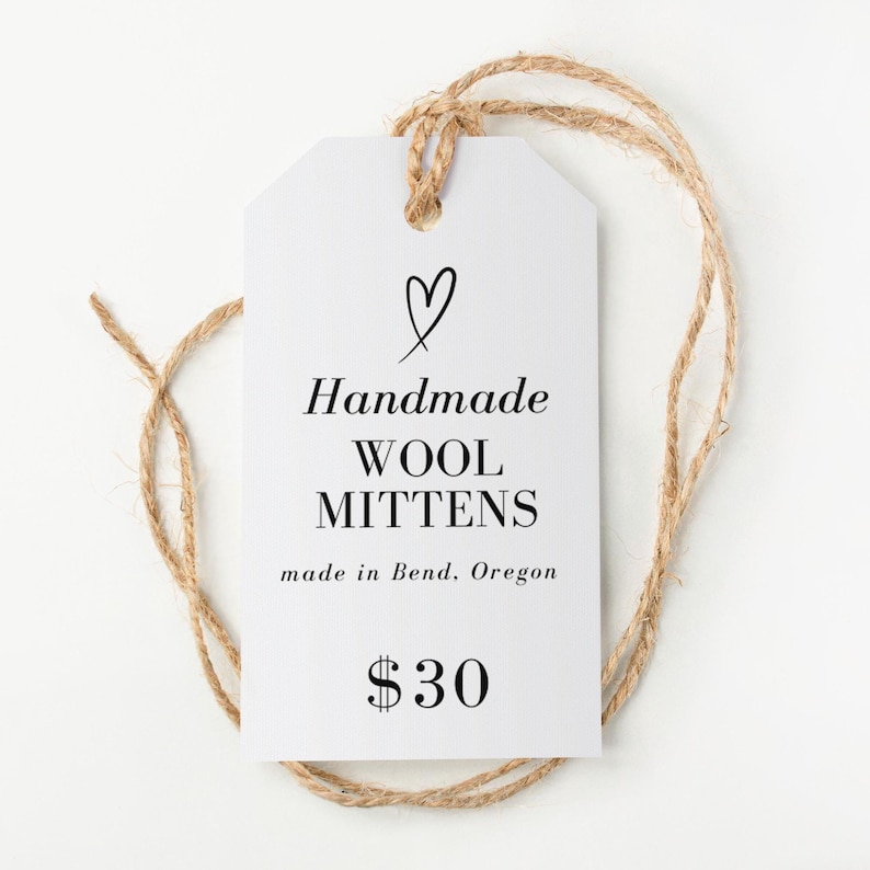 May include: A white tag with a jute string loop features the text "Handmade WOOL MITTENS" with a heart symbol above. The tag also includes "made in Bend, Oregon" and the price.