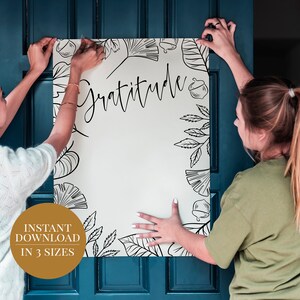 Peut inclure: Deux personnes accrochent une affiche blanche avec des motifs floraux noirs et le mot "Gratitude" sur une porte bleu sarcelle. L'affiche est disponible en t&eacute;l&eacute;chargement instantan&eacute; en trois tailles.