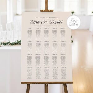 May include: A wedding seating plan displayed on an easel. The cream-coloured sign features the names Cara & Daniel and the wedding date. Guest names are listed under table numbers. The text "4 Sizes Print Today Edit in Canva" is in the upper right corner.