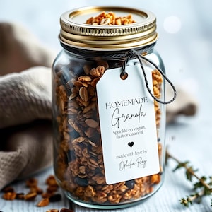 Op de afbeelding: Een glazen pot gevuld met zelfgemaakte granola, met een wit label waarop staat "HOMEMADE Granola Sprinkle on yogurt, fruit or oatmeal made with love by Ophelia Ray".