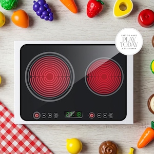 May include: A white toy stovetop with two red hot burners and a digital display that reads "27.88". The stovetop is surrounded by various colorful toy foods, including a red strawberry, a green avocado, a yellow lemon, and a purple bunch of grapes.