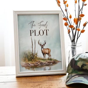 May include: A white framed print with the text "The Food Plot" and a watercolor illustration of a deer standing in a forest clearing.