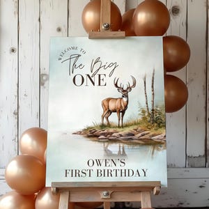 May include: A light blue welcome sign with the text "Welcome to The Big One Owen's First Birthday" and a watercolor illustration of a deer standing in a forest by a lake.