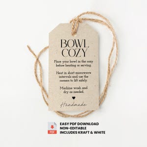 Puede incluir: Una etiqueta beige con las palabras "BOWL COZY" en texto negro, junto con instrucciones de uso. La etiqueta está sujeta a una cuerda de hilo natural. La parte inferior de la etiqueta dice "Handmade".