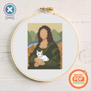 Pode incluir: Ponto cruz da Mona Lisa segurando um gato branco, emoldurado em um bastidor de bordado de madeira. A obra de arte apresenta um design pixelado com um vestido verde, cabelo castanho e um fundo neutro. As palavras "INSTANT PDF DOWNLOAD" estão no canto inferior direito.