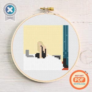 May include: A cross-stitch embroidery in a wooden hoop. The design shows a pixelated image of a person in a bathtub. The background is yellow, with a blue wall and the text "INSTANT PDF DOWNLOAD".