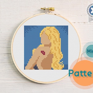 May include: Cross stitch pattern of a woman with blonde hair and a red heart on her shoulder. The pattern is in a hoop and is ready to be stitched.
