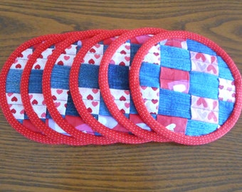 May include: Six round quilted pot holders with a red and white polka dot trim. The pot holders are made of blue denim fabric with pink and white hearts.
