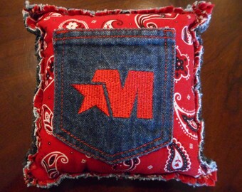 May include: Red and white bandana fabric pillow with a blue denim pocket featuring a red star and the letter "M" embroidered on it.