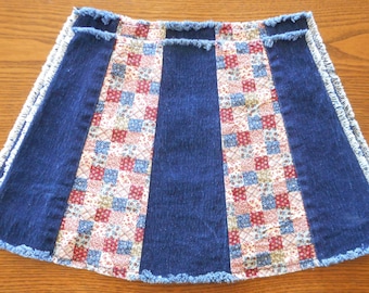 May include: A denim skirt with a patchwork design. The skirt has a frayed hem and is made of blue denim with a white and red patchwork pattern.