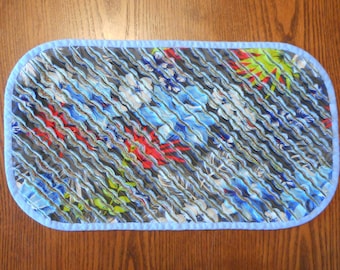 May include: A blue and white floral table runner with a light blue trim. The runner is quilted and has a wavy texture.