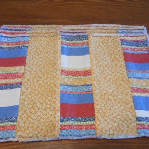 May include: A set of six placemats with a patchwork design. The placemats are made of fabric with a variety of colors and patterns, including red, blue, yellow, and white. The placemats have a frayed edge.
