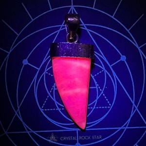 May include: A vibrant pink pendant with a silver-colored bail and trim. The pendant is shaped like a tooth or claw, with a smooth, polished surface. The background is a dark blue with a geometric design and the text "CRYSTAL ROCK STAR".
