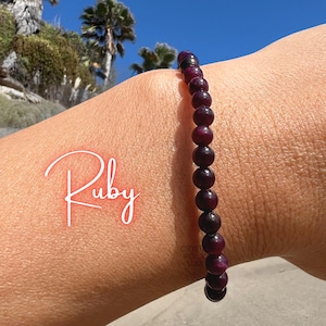 May include: A beaded bracelet featuring small, round, deep red ruby gemstones. The word Ruby is written in a white script font on the left side of the image, and the text Crystal Rock Star is visible in the top right corner of the frame.