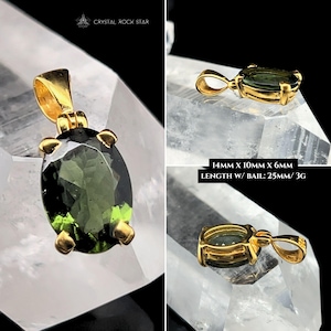 Puede incluir: Un colgante de oro con una piedra preciosa ovalada de color verde oliva. El colgante mide aproximadamente 25 mm de largo con una argolla, y la piedra preciosa mide 14 mm x 10 mm x 6 mm. El colgante se muestra sobre una superficie cristalina transparente.