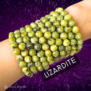 May include: A bracelet made of green and black lizard skin jasper beads. The bracelet is stacked on a person's wrist. The text "Lizarddite" is written in white on a black background.