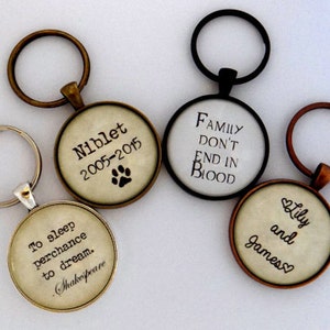 May include: Four different keychains with round glass charms. The charms have different quotes and designs. One keychain has a quote from Shakespeare, another has a quote about family, another has a quote about love, and the last one has a pet's name and dates.