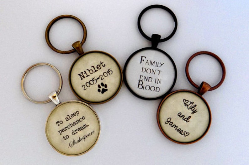 May include: Four different keychains with round glass charms. The charms have different quotes and designs. One keychain has a quote from Shakespeare, another has a quote about family, another has a quote about love, and the last one has a pet's name and dates.