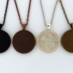 K&ouml;nnte beinhalten: Vier runde Anh&auml;ngerketten mit verschiedenen Kettenfarben. Die Anh&auml;nger sind schwarz, kupfer, silber und bronze.