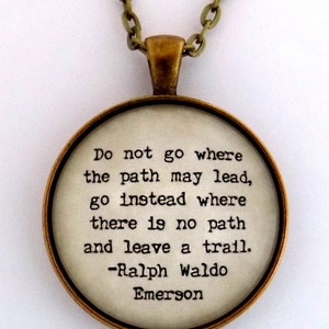 May include: A gold chain necklace with a round pendant featuring a quote by Ralph Waldo Emerson: "Do not go where the path may lead, go instead where there is no path and leave a trail."