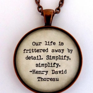 Puede incluir: Un collar de cobre con un colgante redondo que presenta una cita de Henry David Thoreau: "Nuestra vida se desperdicia en detalles. Simplifica, simplifica."
