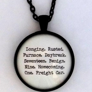 K&ouml;nnte beinhalten: Eine schwarze Kettenkette mit einem runden Glasanh&auml;nger. Der Anh&auml;nger hat wei&szlig;en Text, der lautet: "Longing. Rusted. Furnace. Daybreak. Seventeen. Benign. Nine. Homecoming. One. Freight Car."