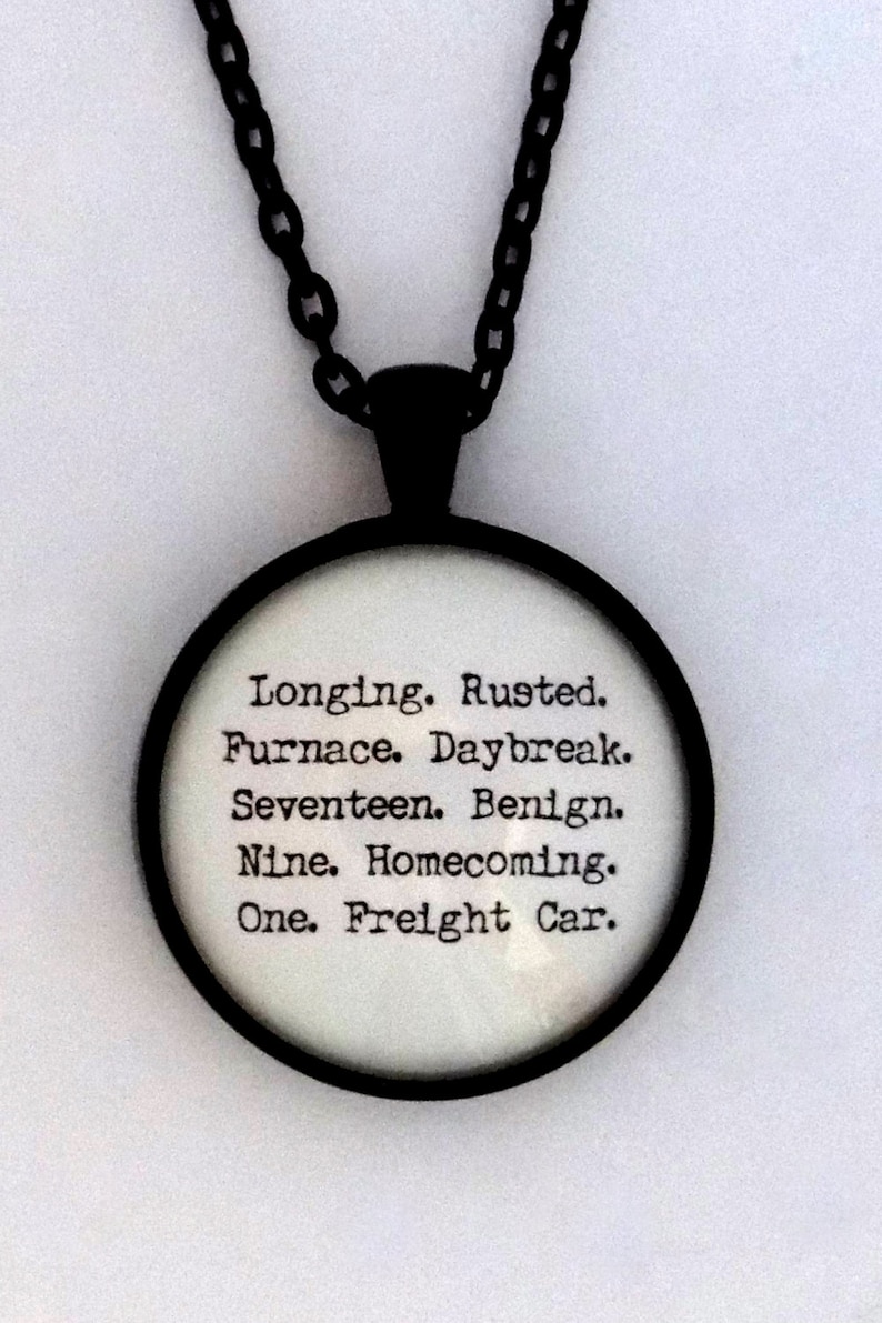 K&ouml;nnte beinhalten: Eine schwarze Kettenkette mit einem runden Glasanh&auml;nger. Der Anh&auml;nger hat wei&szlig;en Text, der lautet: "Longing. Rusted. Furnace. Daybreak. Seventeen. Benign. Nine. Homecoming. One. Freight Car."