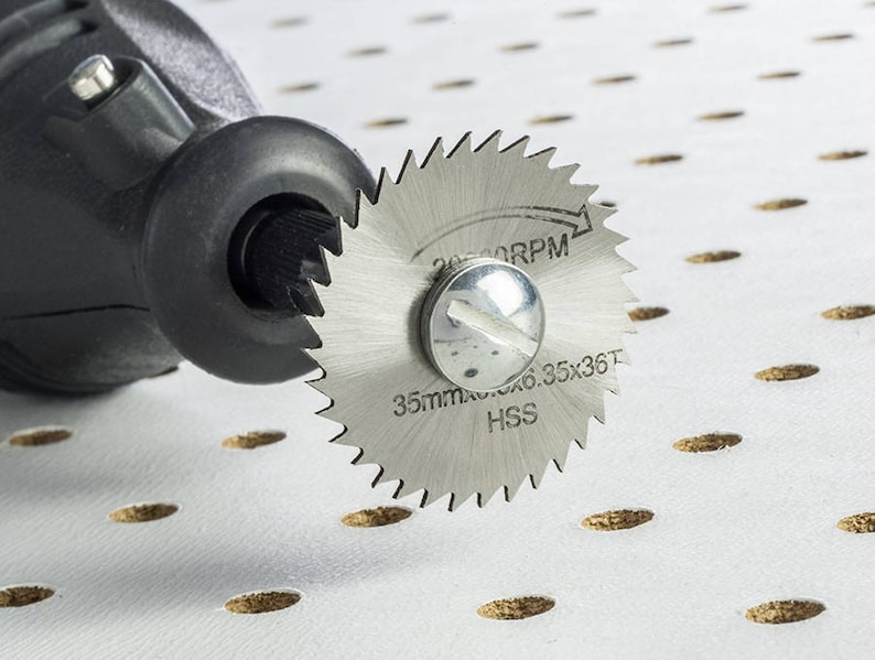 May include: A close-up of a silver rotary tool blade with the text "35mm Max 6.35x35T HSS 20,000 RPM" printed on it. The blade is attached to a black rotary tool.