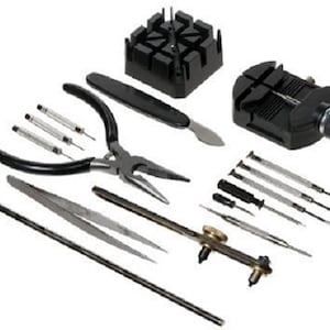 Puede incluir: Un conjunto de herramientas de reparación de relojes, que incluye un soporte de reloj negro, alicates, destornilladores, pinzas, un martillo y un abridor de cajas. Las herramientas están dispuestas sobre una superficie blanca.